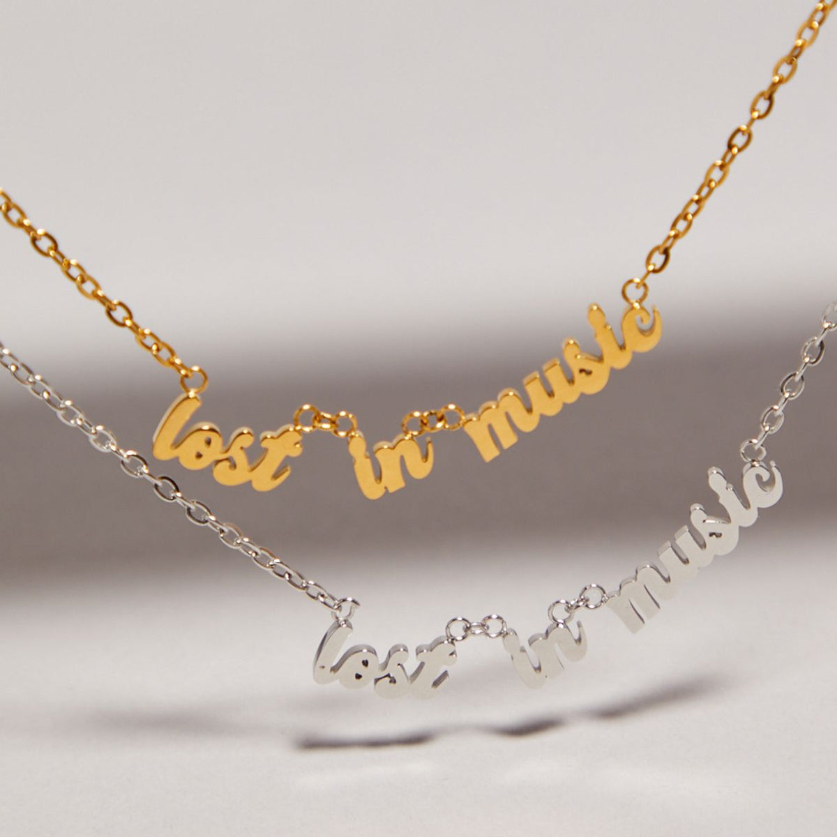 Two necklaces with 'lost in music' text on a neutral background