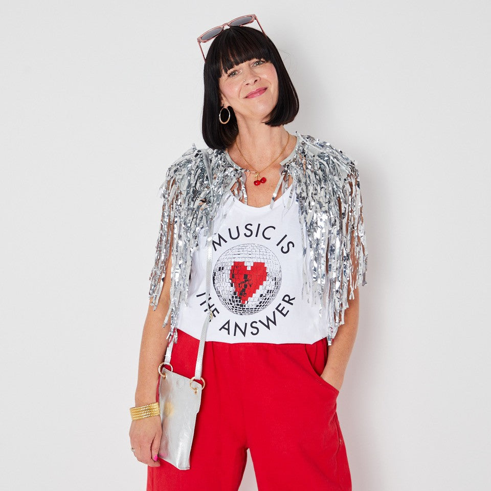 Woman wearing a vest with 'Music is the Answer' text and a red skirt against a wooden background.