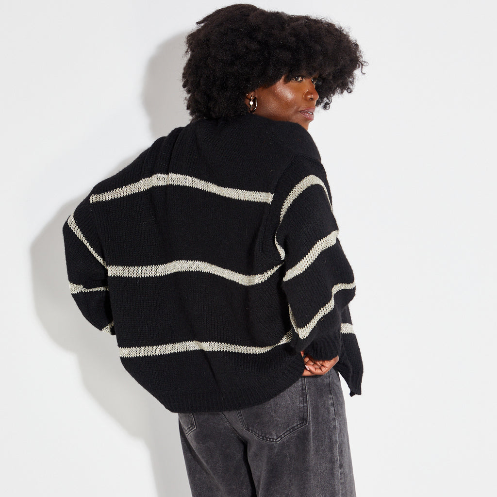 Woman wearing a black and white striped shirt with a black gold metallic stripe cardigan on a white background