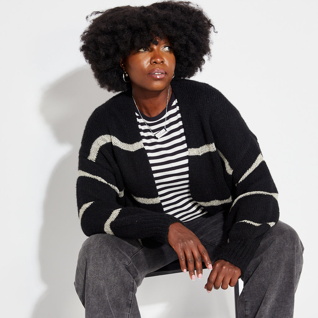 Woman wearing a black and white striped shirt with a black gold metallic stripe cardigan on a white background