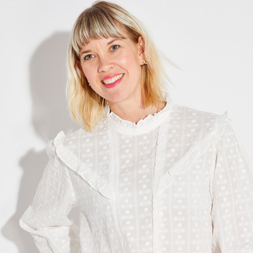 Person wearing a white blouse with ruffled details on a plain background