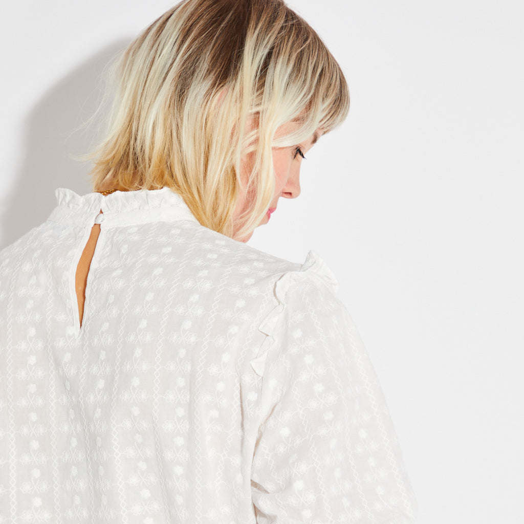 Person wearing a white blouse with ruffled details on a plain background