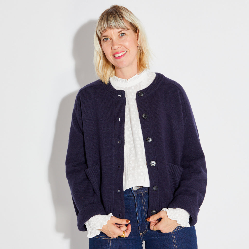 Woman wearing a navy blue cardigan over a white blouse with a plain background