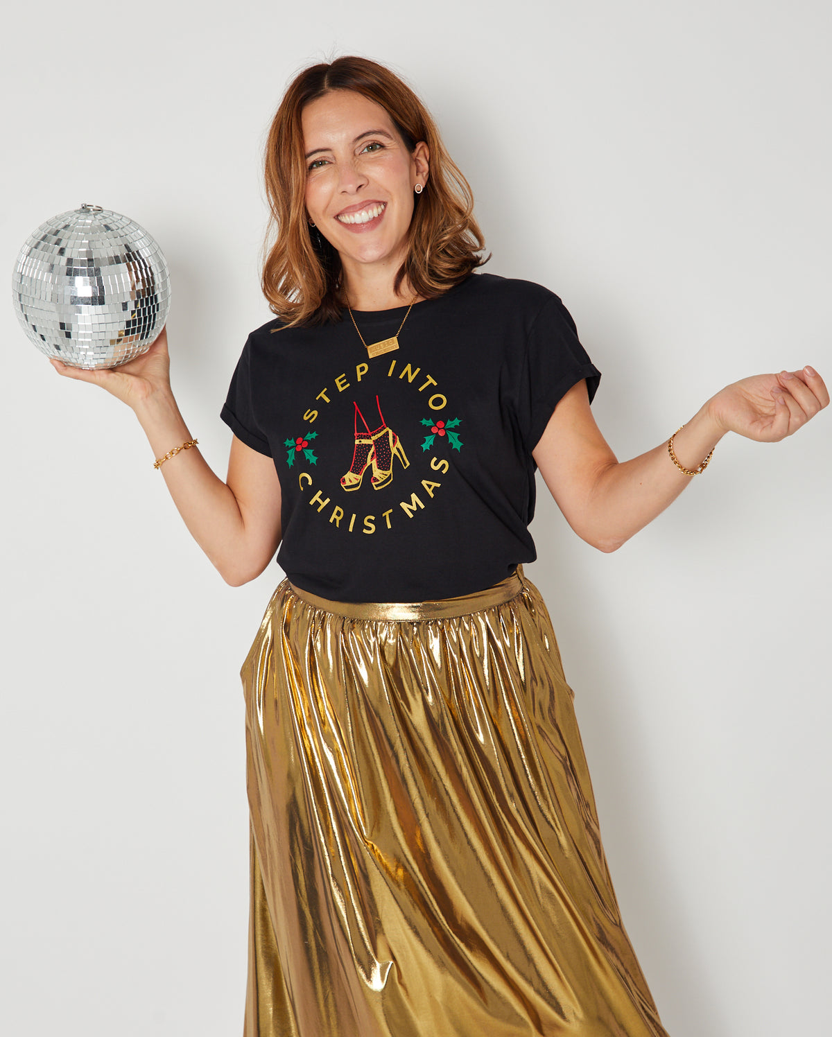 black graphic t-shirt  'STEP INTO CHRISTMAS'  with a gold skirt, holding a silver disco bal