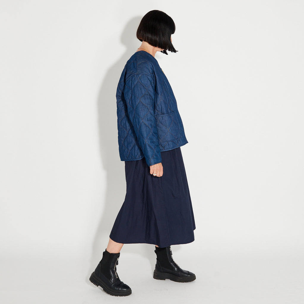 Person wearing a blue quilted denim jacket and navy skirt on a white background
