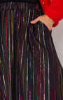 Close-up of a person wearing a black skirt with vertical metallic rainbow stripes in red, purple, gold, and silver, 