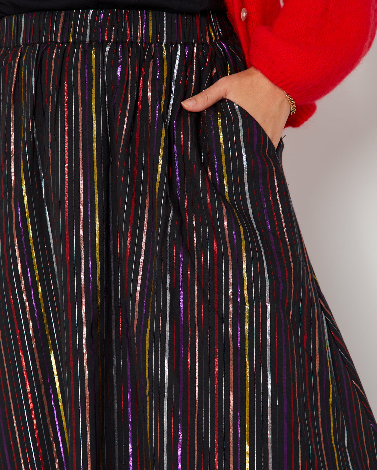 Close-up of a person wearing a black skirt with vertical metallic rainbow stripes in red, purple, gold, and silver, 