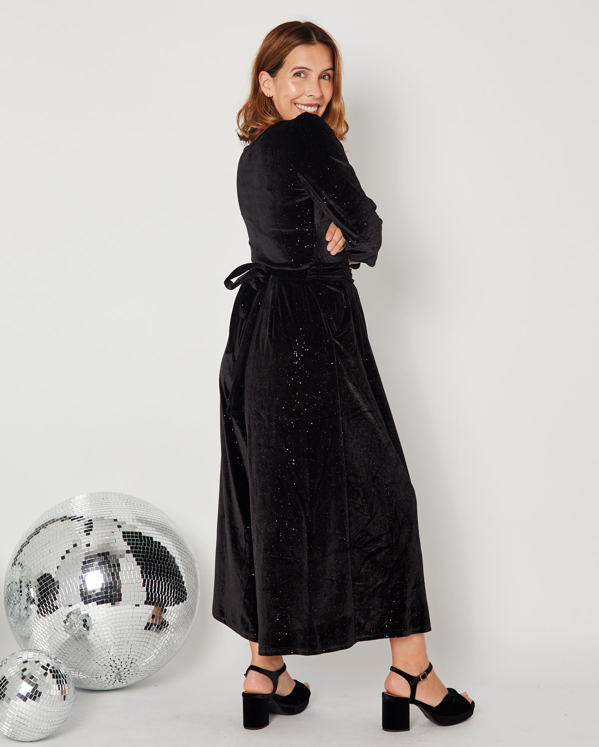 side view of Black Rainbow Sparkle Jumpsuit with heels and showing the tie back waist