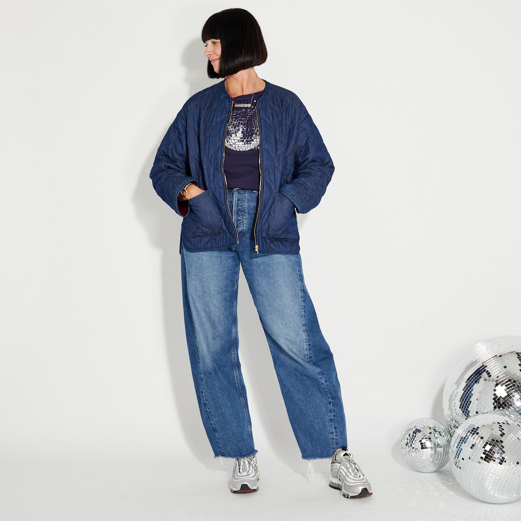 Person wearing a blue denim quilted jacket and jeans with disco balls on a white background