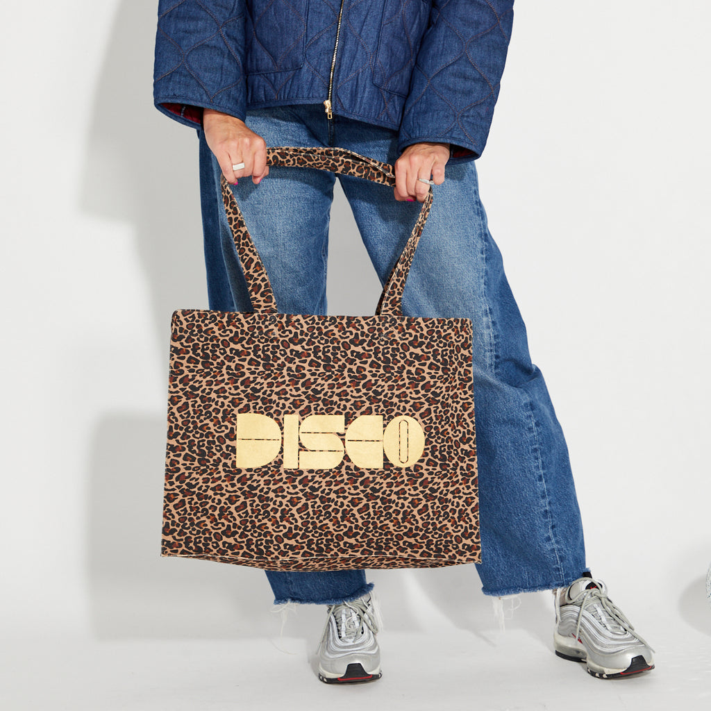 Person holding a leopard print tote bag with gold 'DISCO' text against a white background
