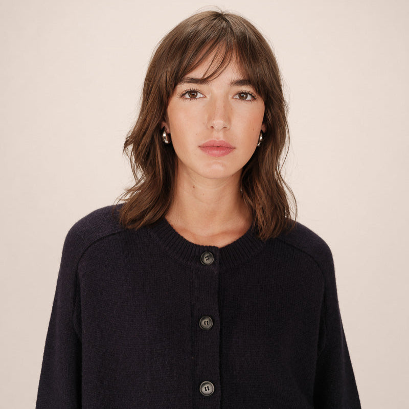 Woman wearing a dark blue cardigan against a plain background