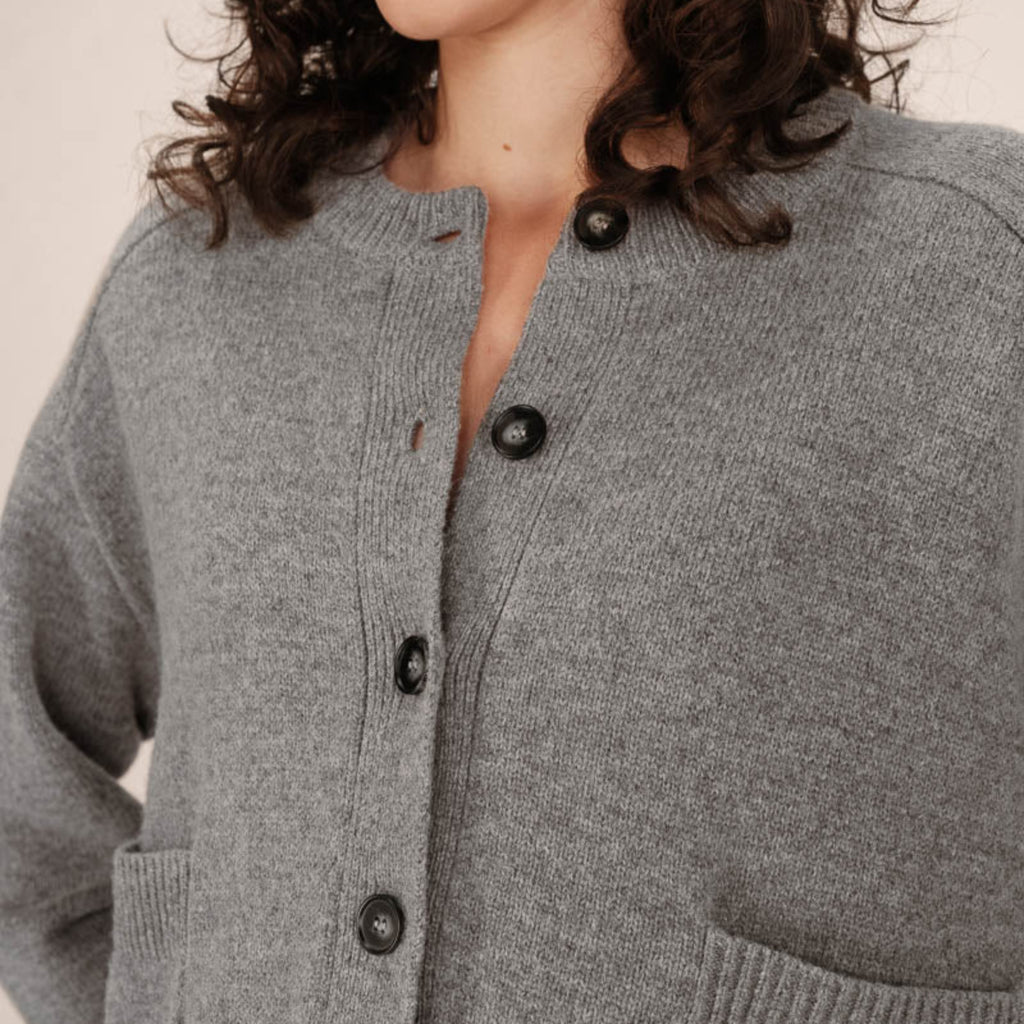 Close-up of a person wearing a gray cardigan with black buttons on a neutral background