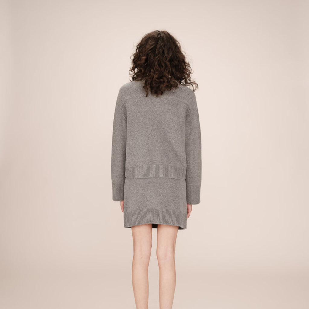 Person wearing a grey cardigan and skirt on a beige background