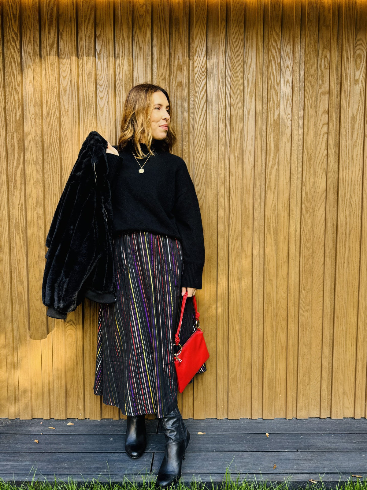 multicoloured skirt with black jumper and red bag