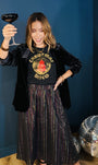 A woman posing in a black velvet blazer over a black graphic t-shirt that reads 'Christmas Disco' in gold and red, paired with a rainbow metallic a line skirt.