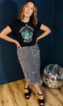 A woman posing in a black graphic t-shirt that reads 'Christmas Disco' with a green tree, paired with a sparkly silver sequin pencil skirt and black heels.