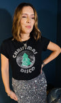 A woman wearing a black graphic t-shirt with a silver and green 'Christmas Disco' disco ball design, paired with a silver sequined skirt.