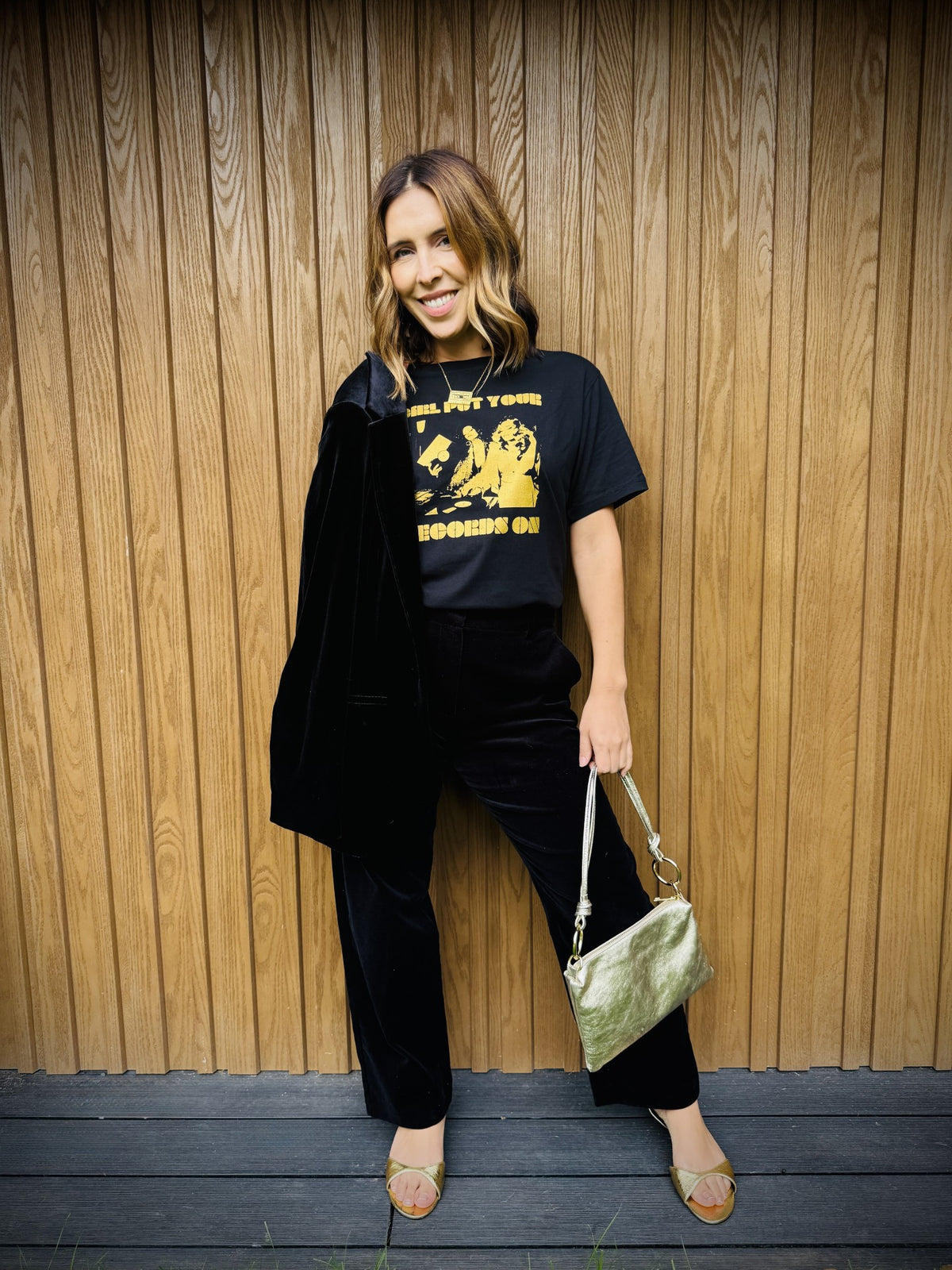 girl put your records on black tshirt with black suit and gold bag