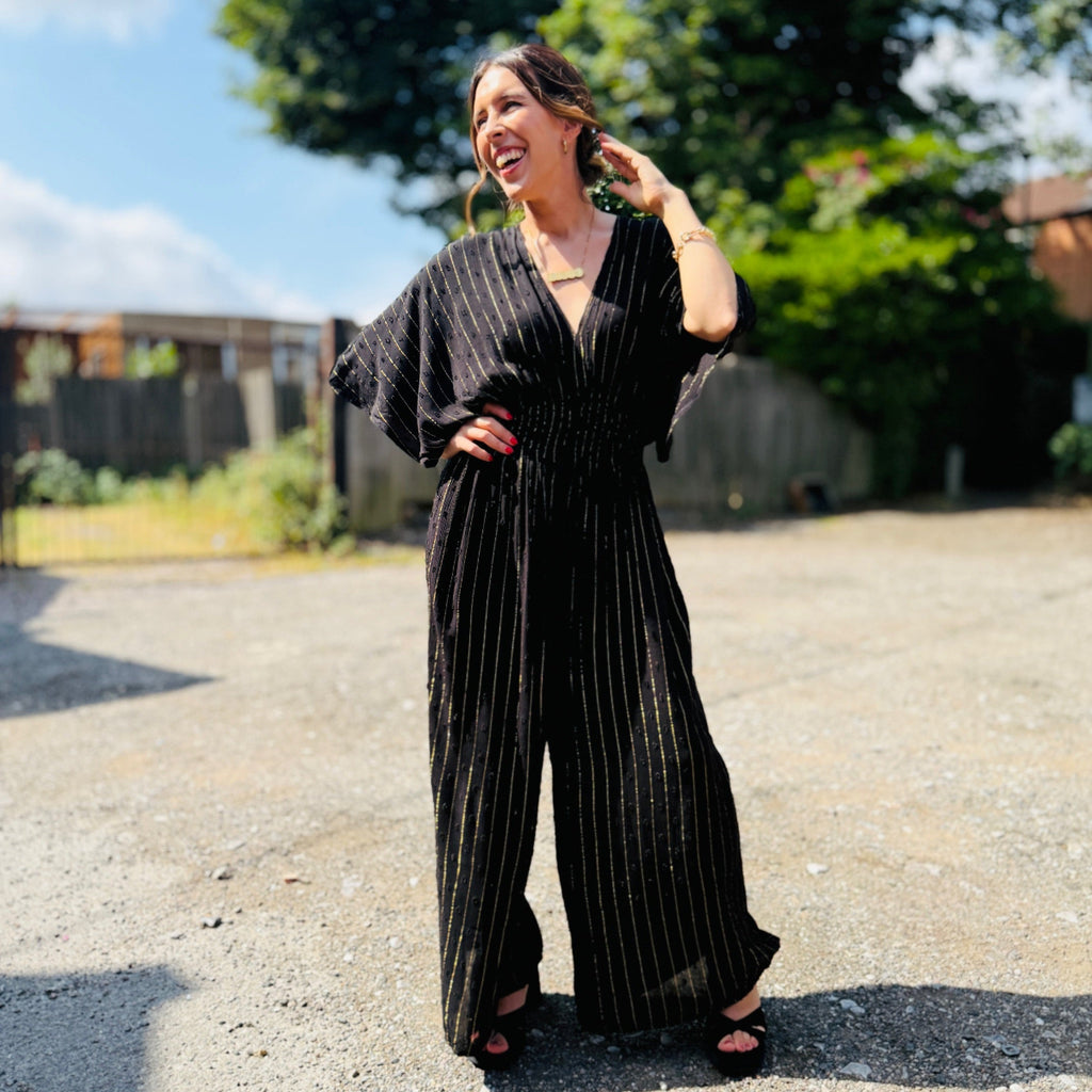 Woman wearing a black pinstripe jumpsuit outdoors on a sunny day.