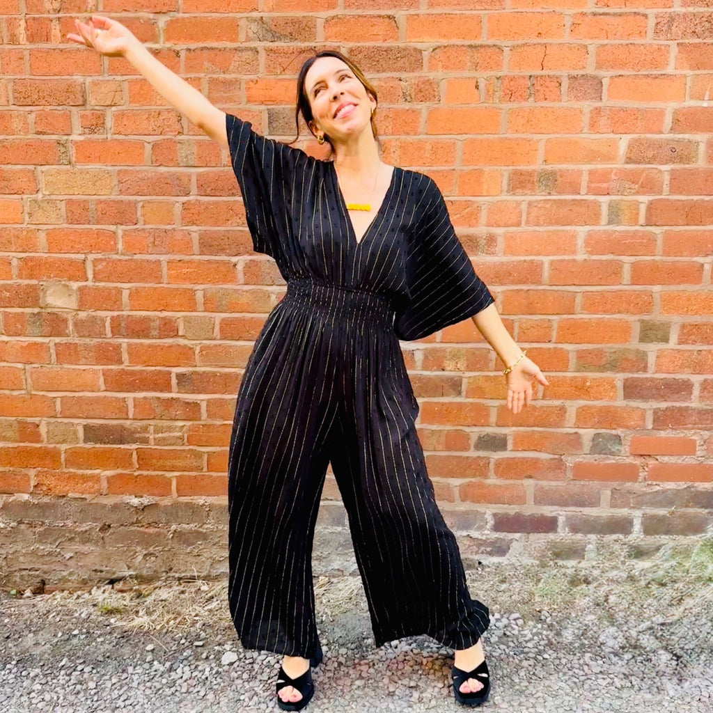Woman in a black pinstripe jumpsuit standing against a brick wall.