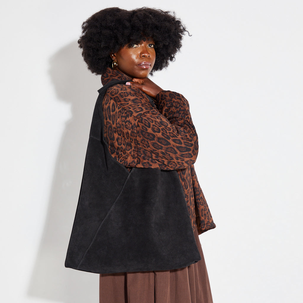 Woman carrying a black slouchy bag and wearing a leopard print top against a white background