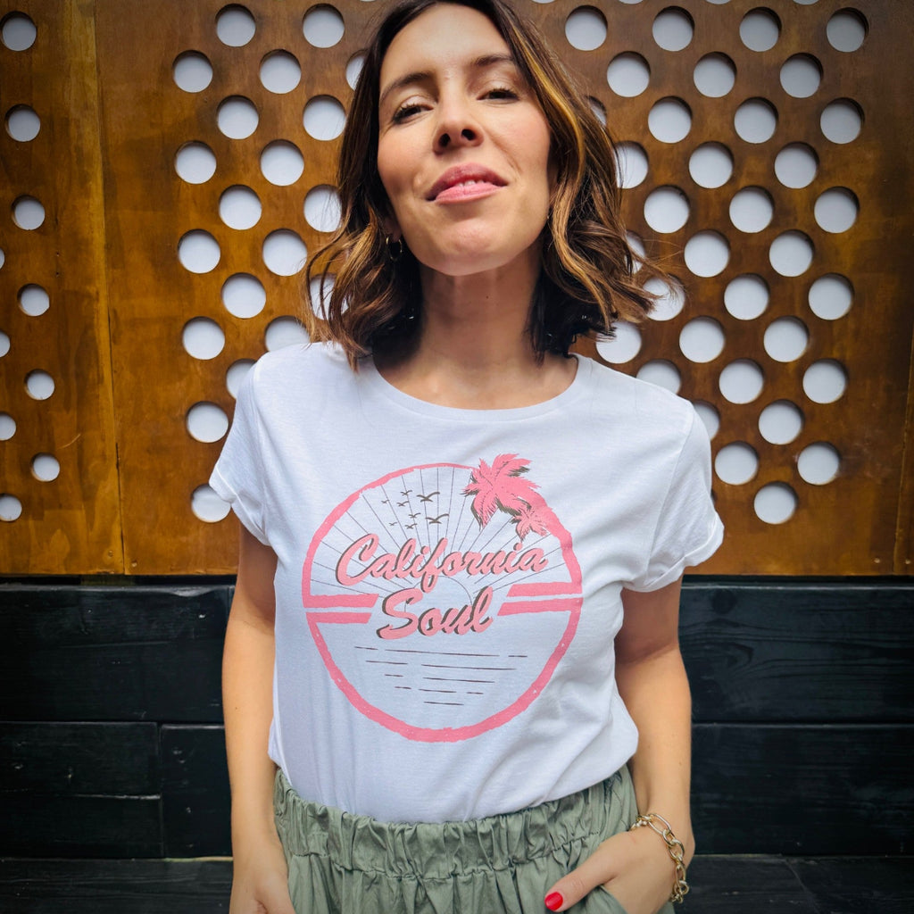 Woman wearing a white t-shirt with pink 'California Cool' design against a wooden panel background