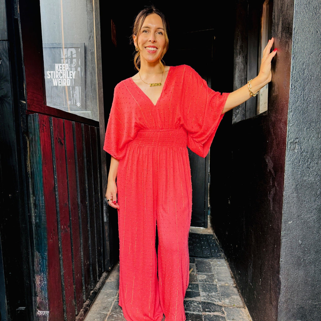 Woman in a red jumpsuit standing in a narrow alleyway.