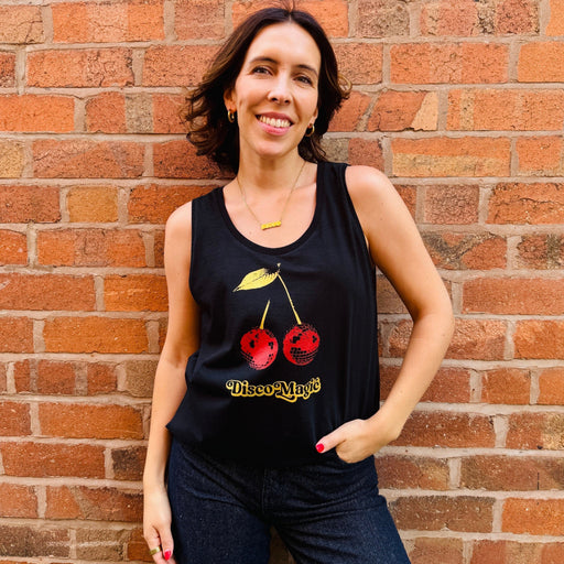 Woman wearing a black tank top with red cherries and 'Disco Magic' text against a brick wall.
