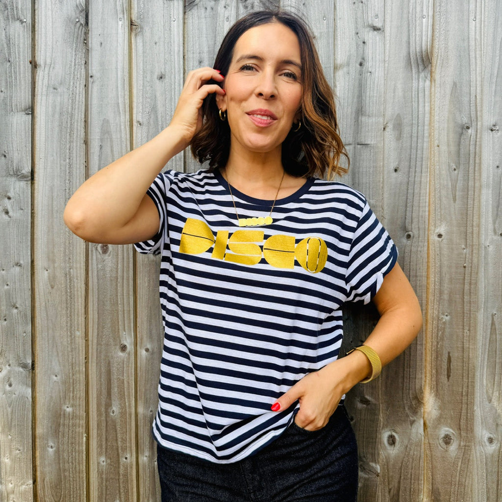 Woman wearing a black and white striped t-shirt with yellow graphic design against a wooden fence.