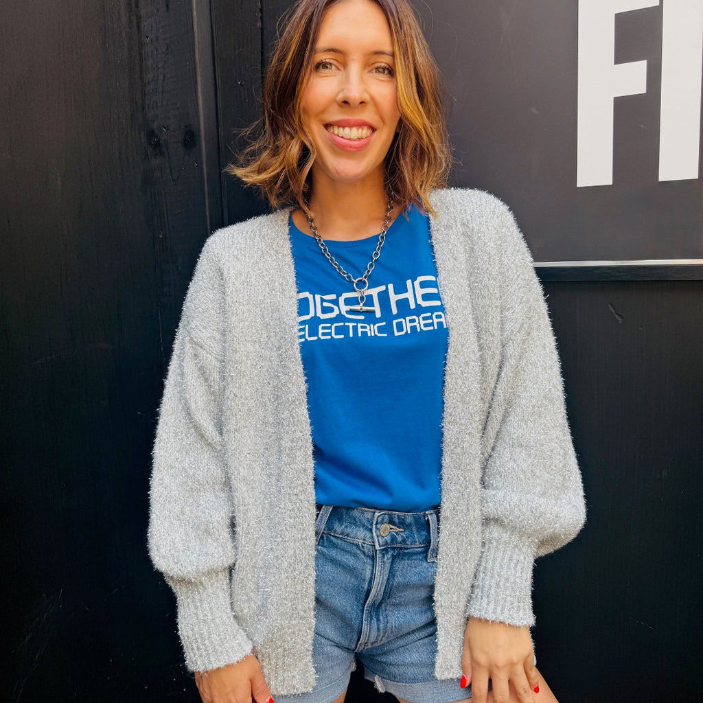 Woman wearing a blue t-shirt with text and a gray cardigan, standing against a black background.