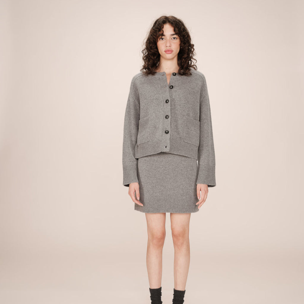 Woman wearing a gray cardigan and skirt set on a beige background