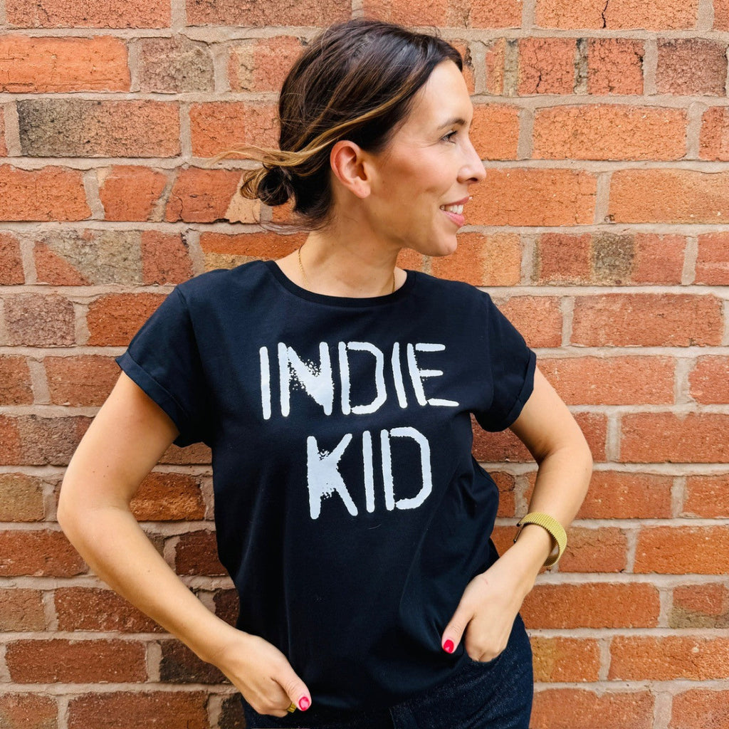 Woman wearing a black t-shirt with 'INDIE KID' text against a brick wall.