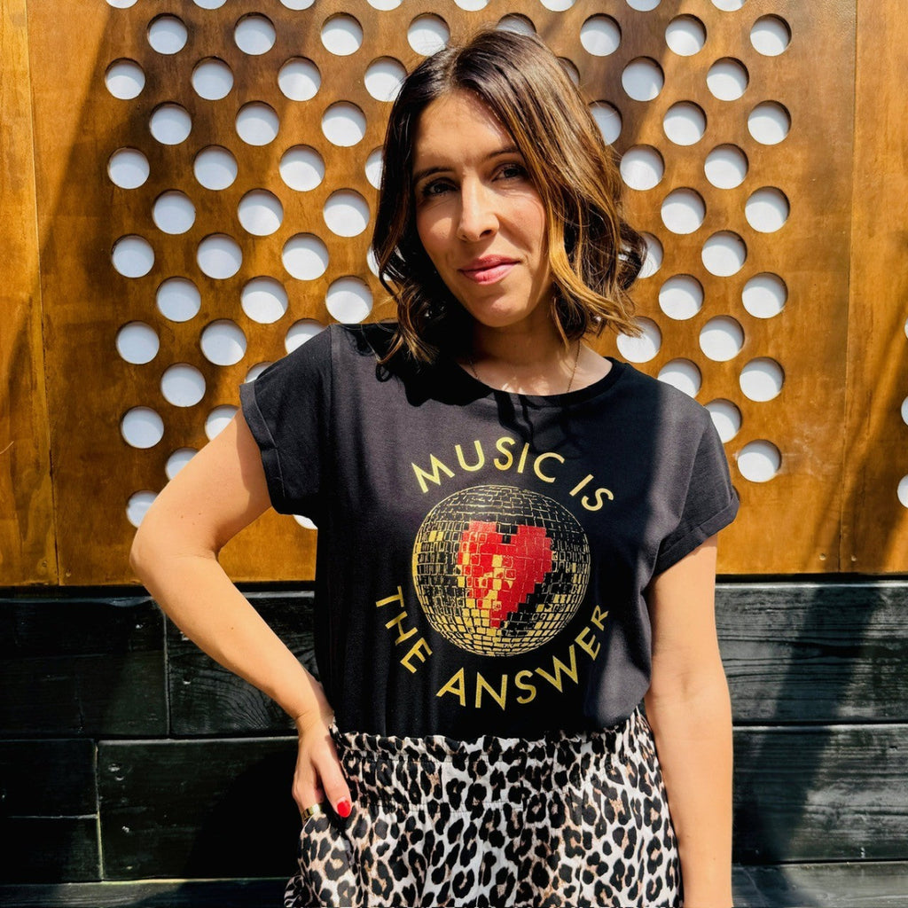 Woman wearing a black t-shirt with 'Music is the Answer' design against a wooden wall.