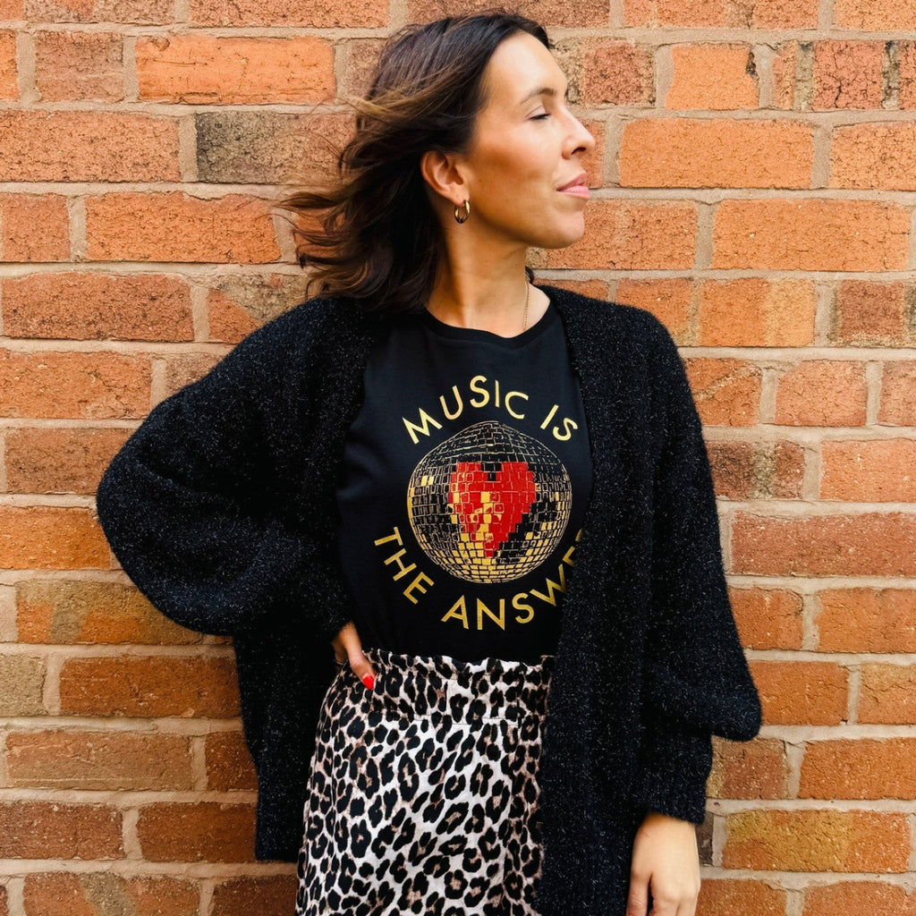 Woman wearing a black sweater with 'Music is the Answer' text against a brick wall.