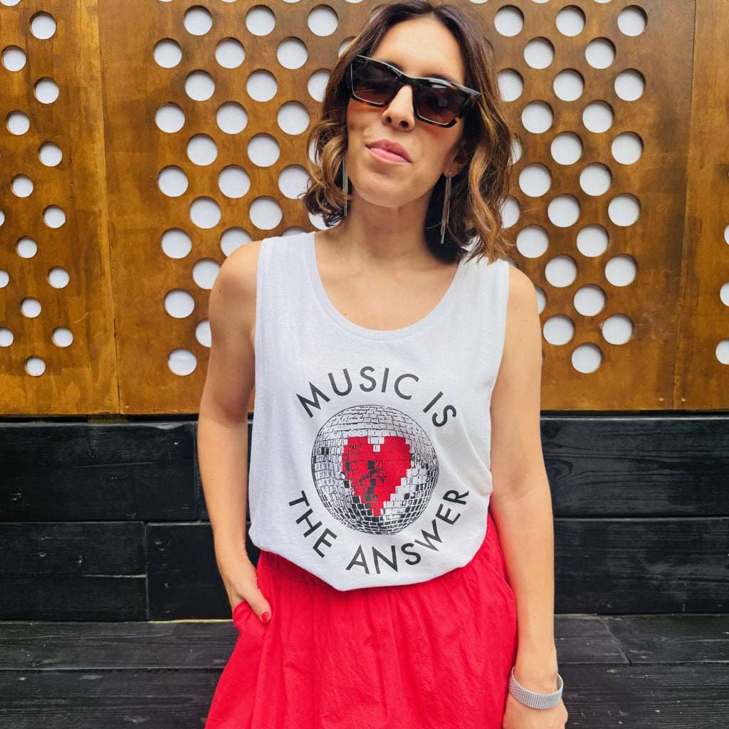 Woman wearing a vest with 'Music is the Answer' text and a red skirt against a wooden background.