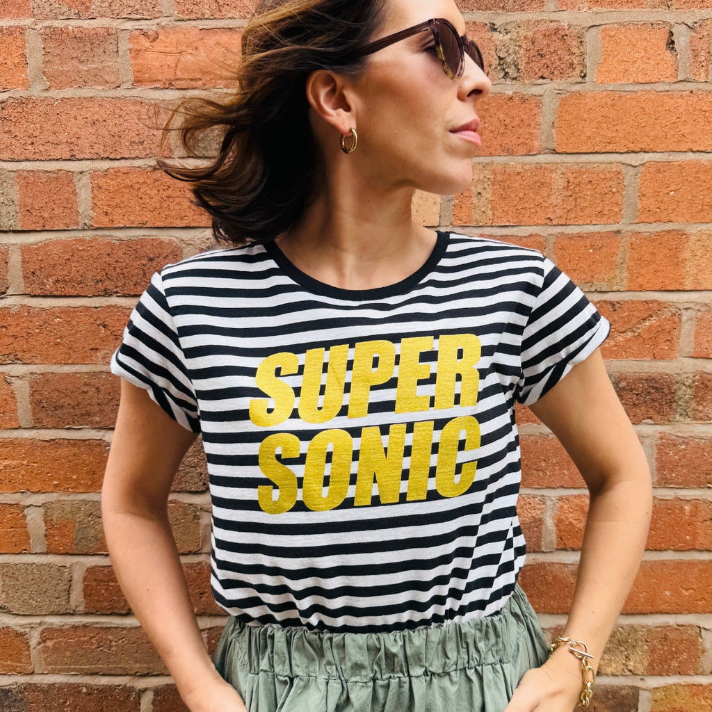 Woman wearing a black and white striped t-shirt with 'Supersonic' text against a brick wall.