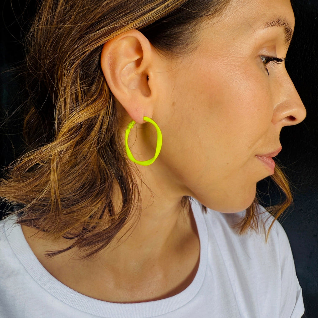 Close-up of a person wearing a neon green hoop earring against a dark background